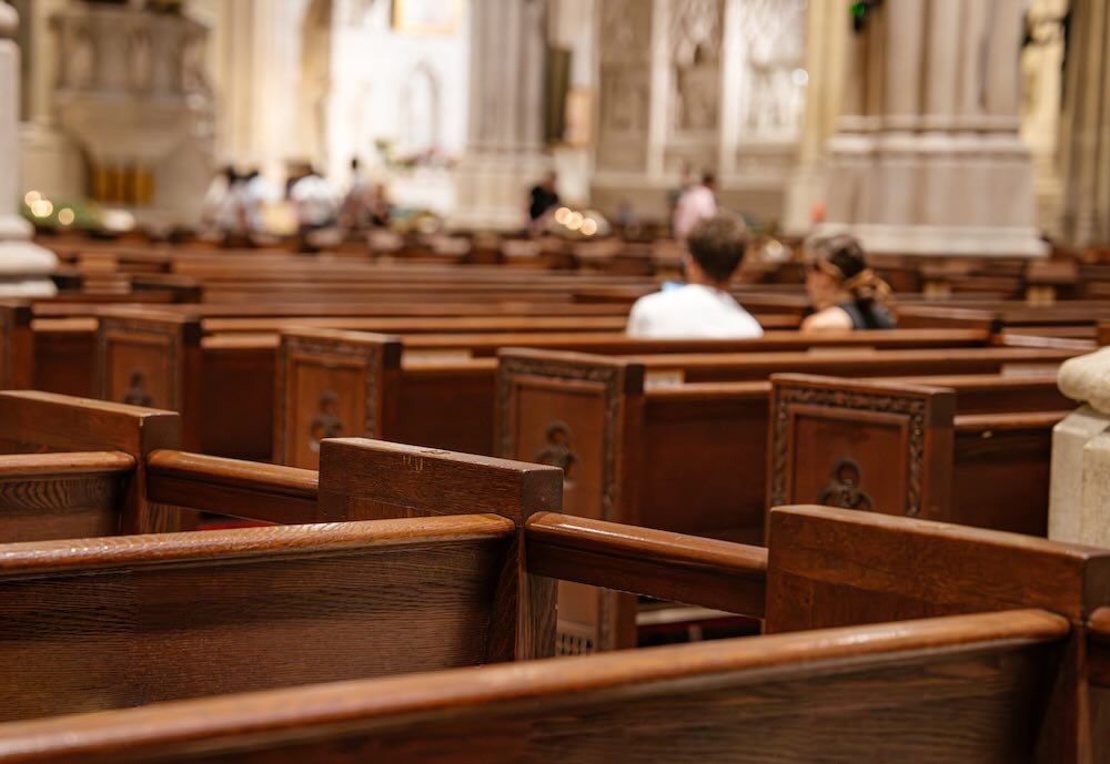 Wooden church pews fill the foreground, leading to a softly lit cathedral interior